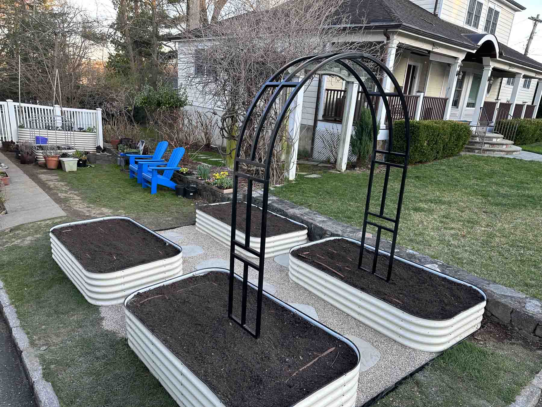 Four new raised metal garden beds filled with fresh soil and a black arched trellis, photographed in early spring before anything has been planted